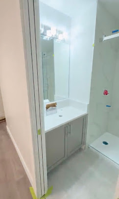 Bathroom with a light vanity, pale walls, a glass shower enclosure, and masking tape.