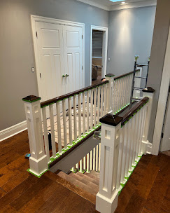 White staircase spindles and posts with dark wood handrails beside grey hallway walls.